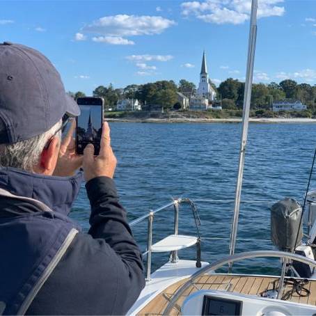 Eine Person auf einem Segelboot peilt eine Kirchturmspitze an zur Entfernungsbestimmunge