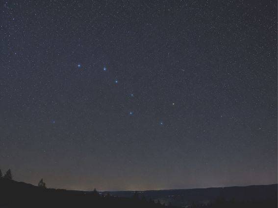 Ein Sternenhimmel mit sichtbarer Konstellation über einer dunklen Berggrenze.